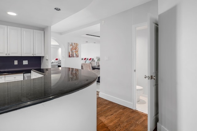 kitchen featuring dark stone counters, kitchen peninsula, dark hardwood / wood-style flooring, and white cabinets