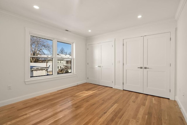 unfurnished bedroom featuring ornamental molding, two closets, and light wood-type flooring