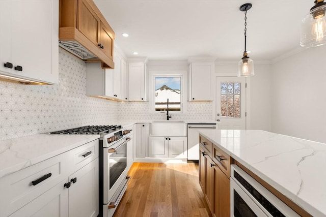 kitchen featuring stainless steel range with gas stovetop, light stone counters, dishwasher, white cabinets, and pendant lighting