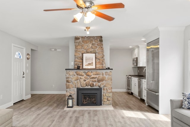 living room with a stone fireplace, light hardwood / wood-style flooring, and ceiling fan