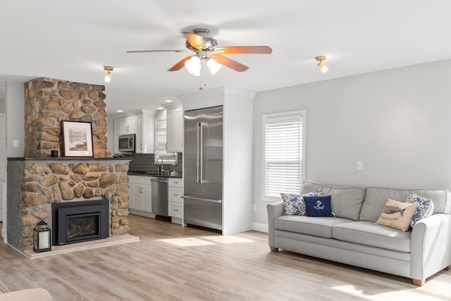 living room featuring sink, a stone fireplace, light hardwood / wood-style flooring, and ceiling fan