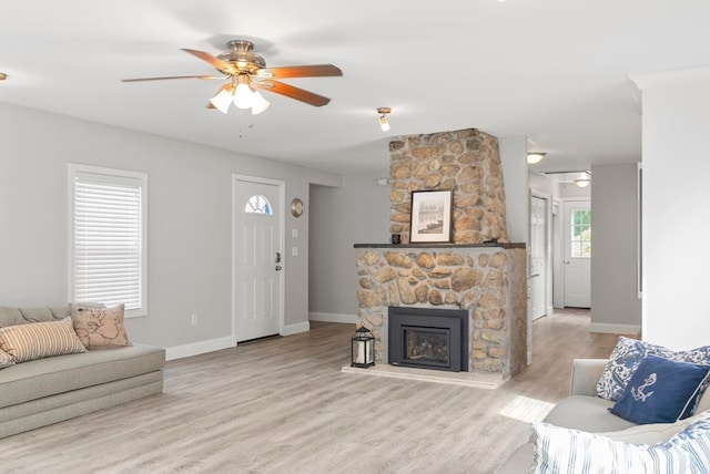 living room with ceiling fan, a stone fireplace, and light wood-type flooring