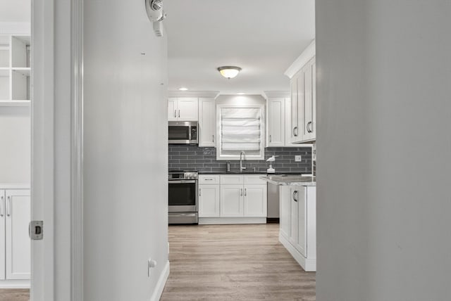 kitchen with light hardwood / wood-style floors, sink, backsplash, white cabinets, and appliances with stainless steel finishes