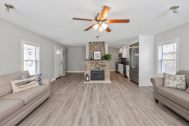 living room featuring ceiling fan, a stone fireplace, light hardwood / wood-style floors, and a wealth of natural light