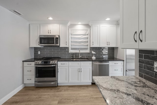 kitchen with light stone counters, sink, white cabinetry, appliances with stainless steel finishes, and backsplash