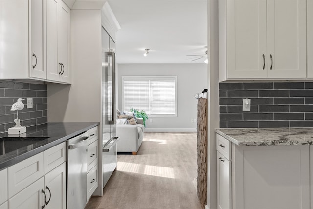 kitchen featuring light wood-type flooring, dark stone countertops, stainless steel appliances, backsplash, and white cabinetry