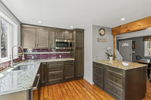 kitchen featuring stainless steel appliances, a peninsula, a sink, tasteful backsplash, and light wood-style floors