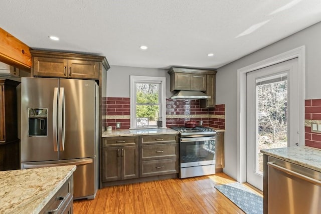 kitchen with light wood-type flooring, decorative backsplash, under cabinet range hood, and appliances with stainless steel finishes