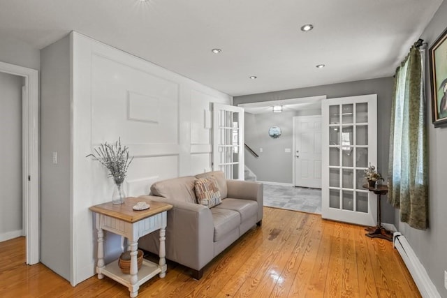 living area featuring recessed lighting, baseboard heating, light wood-type flooring, baseboards, and stairs