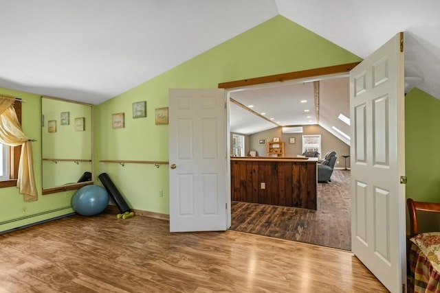 exercise area featuring a baseboard heating unit, a wall unit AC, baseboards, lofted ceiling, and wood finished floors