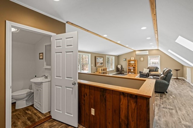 interior space featuring lofted ceiling with skylight, a sink, a wall mounted AC, light countertops, and dark wood-type flooring