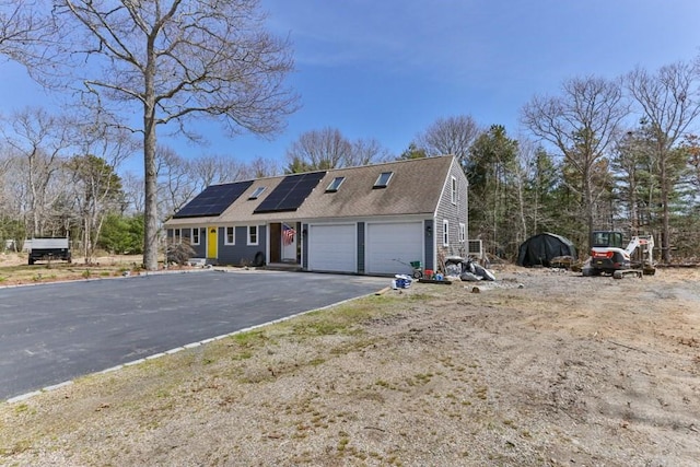 view of front facade featuring roof mounted solar panels, a shingled roof, and driveway