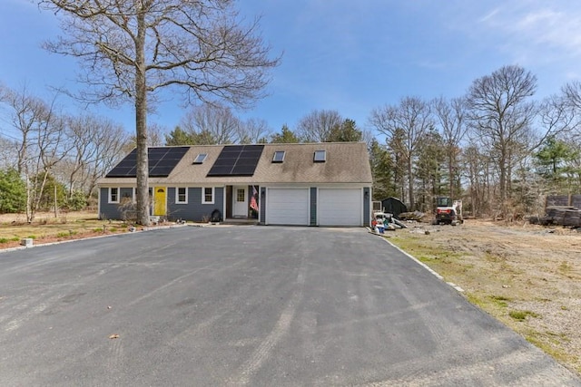colonial inspired home featuring roof mounted solar panels, driveway, roof with shingles, and a garage