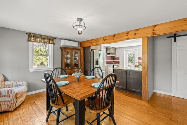 dining area with light wood-type flooring, baseboards, an AC wall unit, and a barn door