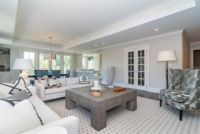 living room featuring light hardwood / wood-style floors, a tray ceiling, ornamental molding, and french doors