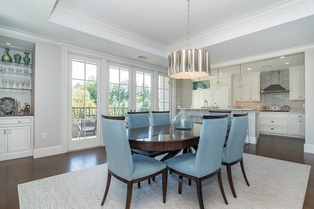 dining space with dark wood-type flooring, a tray ceiling, and ornamental molding