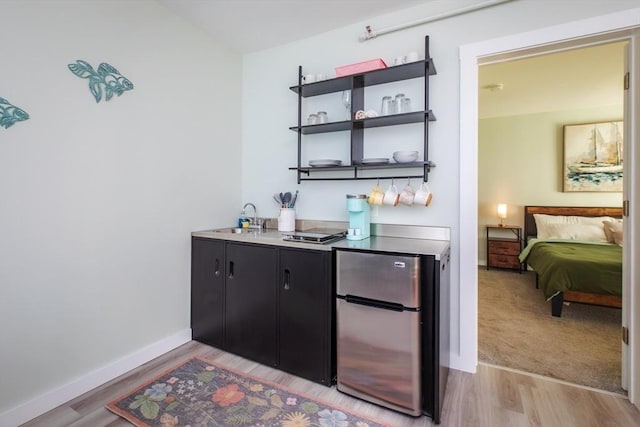 bar with light wood-type flooring, wet bar, a sink, and freestanding refrigerator