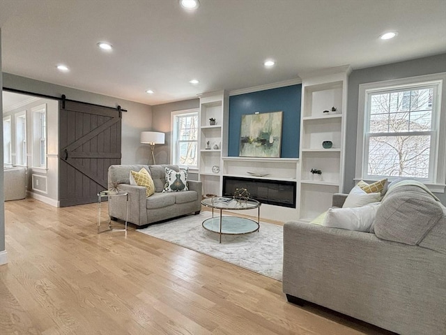 living area featuring a glass covered fireplace, a barn door, recessed lighting, and light wood finished floors