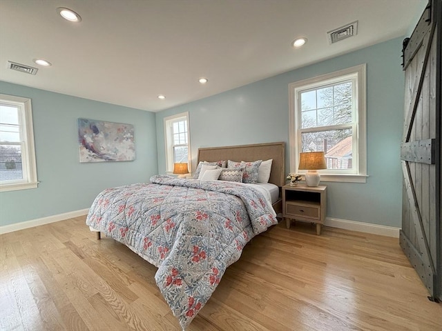 bedroom with a barn door, baseboards, visible vents, and light wood-style flooring