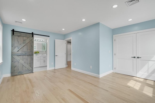 unfurnished bedroom with a barn door, visible vents, and light wood finished floors