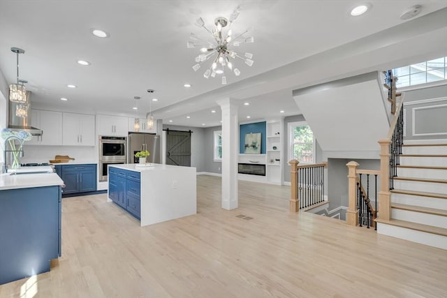 kitchen with light wood finished floors, light countertops, a barn door, appliances with stainless steel finishes, and blue cabinets