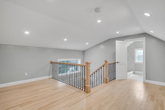 corridor featuring wood finished floors, baseboards, lofted ceiling, recessed lighting, and an upstairs landing