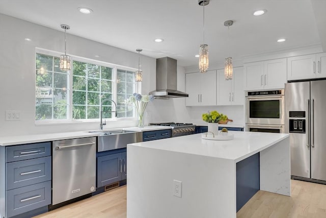 kitchen with light wood-type flooring, a sink, wall chimney range hood, stainless steel appliances, and light countertops