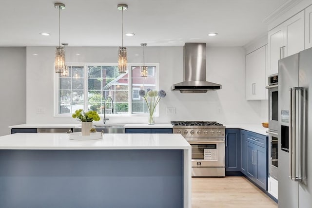 kitchen with wall chimney range hood, high end appliances, blue cabinetry, and a sink