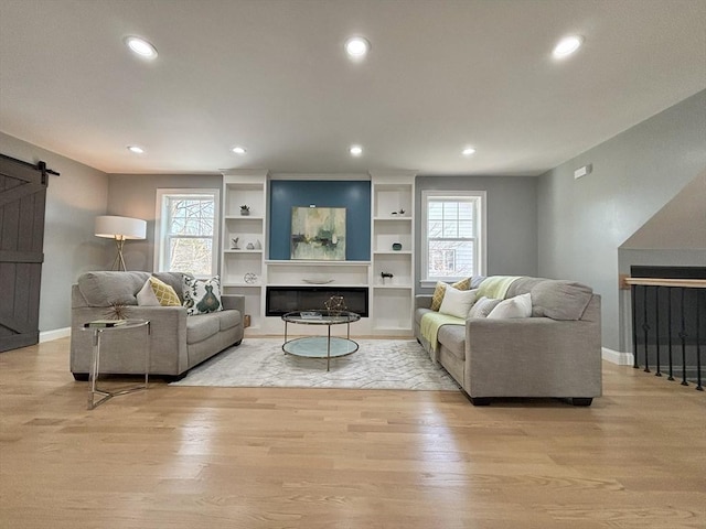 living room featuring light wood finished floors, a glass covered fireplace, recessed lighting, and a barn door