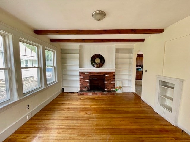 unfurnished living room featuring light hardwood / wood-style flooring, a brick fireplace, and beam ceiling