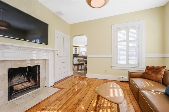 113 Taylor St Unit 1, Waltham, MA 02453 - living area featuring visible vents, light wood-style floors, baseboard heating, a tiled fireplace, and arched walkways