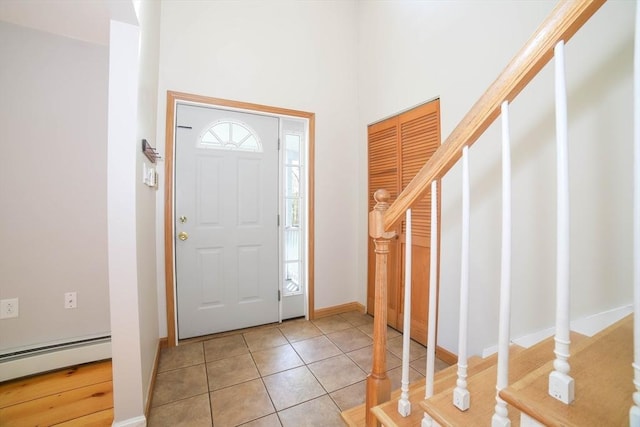 entrance foyer with a towering ceiling, stairway, light tile patterned floors, baseboards, and a baseboard heating unit