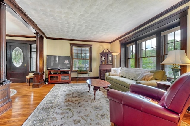 living room with ornate columns, healthy amount of natural light, wood finished floors, crown molding, and baseboards