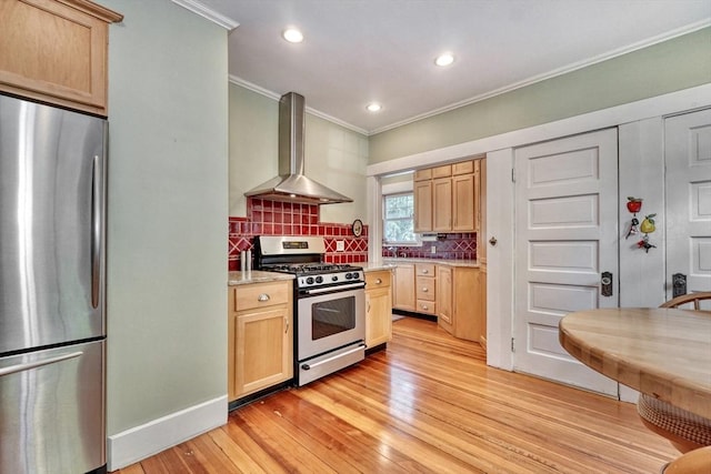 kitchen with appliances with stainless steel finishes, wall chimney range hood, crown molding, light brown cabinets, and light wood-style flooring