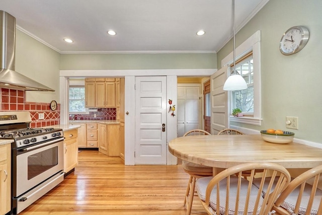 kitchen with gas stove, wall chimney exhaust hood, light brown cabinetry, crown molding, and light wood-type flooring