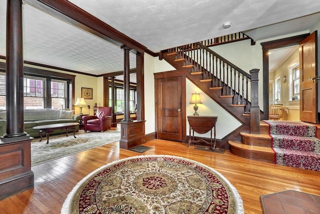 entryway featuring ornate columns, plenty of natural light, ornamental molding, wood finished floors, and stairs