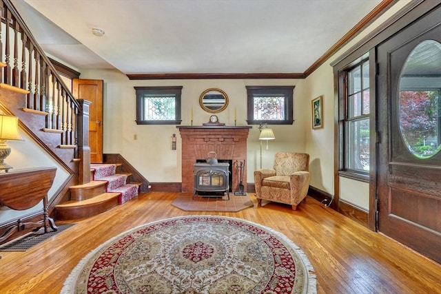 sitting room featuring a wood stove, wood-type flooring, stairs, baseboards, and ornamental molding
