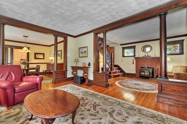 living area with ornate columns, hardwood / wood-style flooring, a wood stove, and ornamental molding