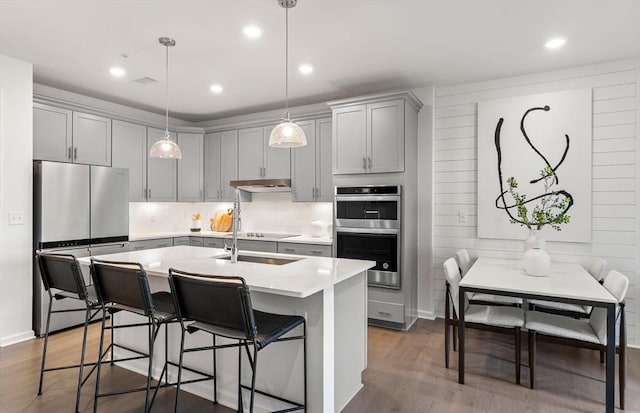 kitchen with gray cabinets, a breakfast bar area, hanging light fixtures, stainless steel appliances, and dark hardwood / wood-style floors