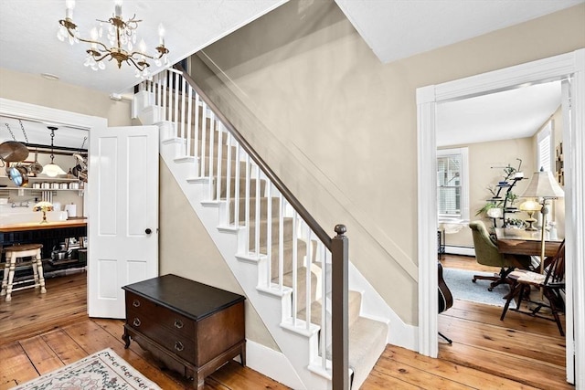 staircase featuring a baseboard radiator, hardwood / wood-style floors, and a notable chandelier