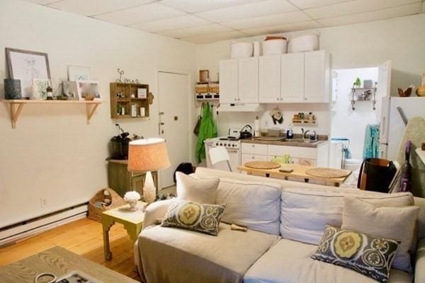 interior space featuring a paneled ceiling, light wood-type flooring, and a baseboard heating unit