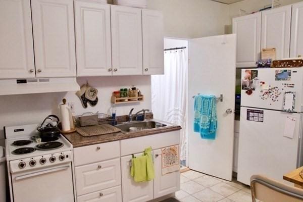 kitchen featuring sink, white appliances, dark stone countertops, white cabinets, and light tile patterned flooring