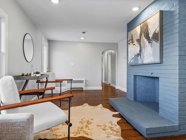 living area with dark wood-type flooring, radiator, and a brick fireplace