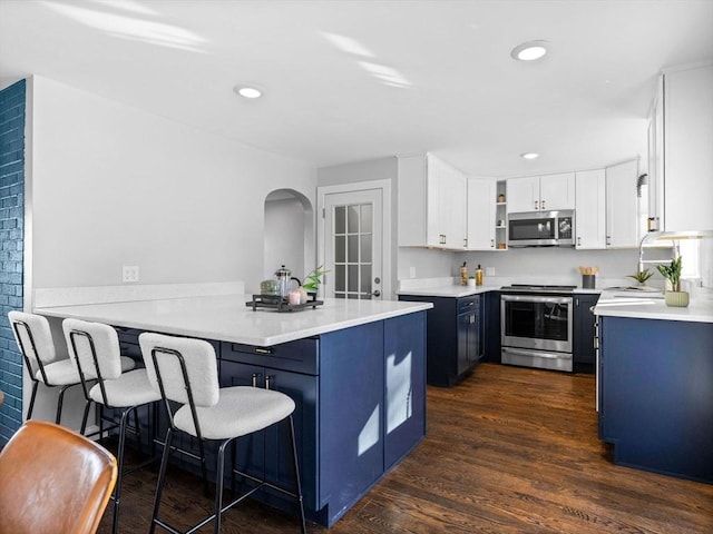 kitchen featuring a kitchen bar, appliances with stainless steel finishes, dark hardwood / wood-style flooring, kitchen peninsula, and white cabinets