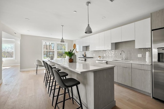 kitchen featuring light wood finished floors, decorative backsplash, appliances with stainless steel finishes, a center island, and a sink