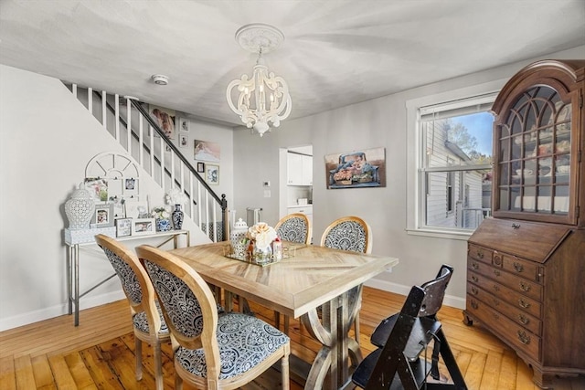 dining space featuring baseboards, light wood finished floors, stairs, and a notable chandelier