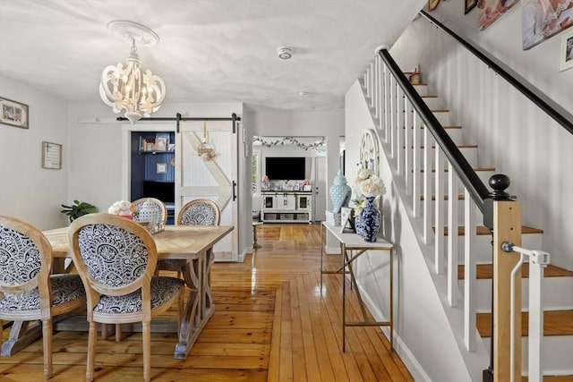 dining space with an inviting chandelier, hardwood / wood-style flooring, a barn door, and stairs
