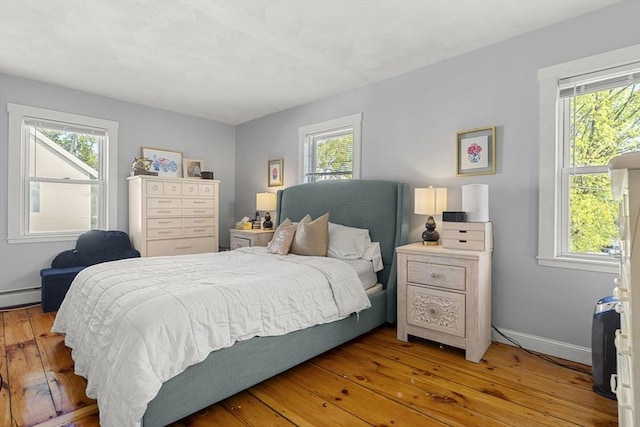 bedroom featuring light wood-type flooring, baseboards, baseboard heating, and multiple windows