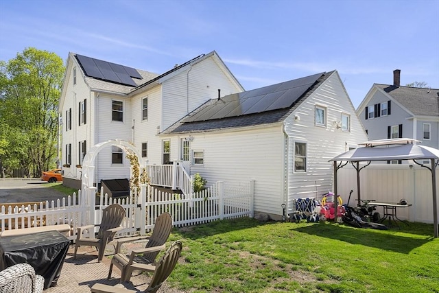 back of house with solar panels, a gazebo, fence, a yard, and a shingled roof