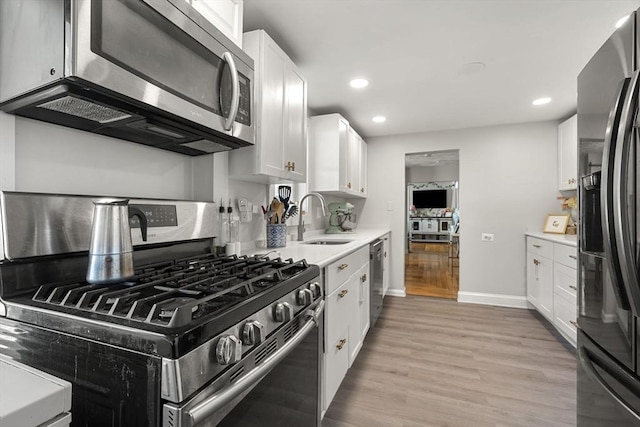 kitchen with a sink, light wood-style floors, light countertops, stainless steel appliances, and white cabinetry